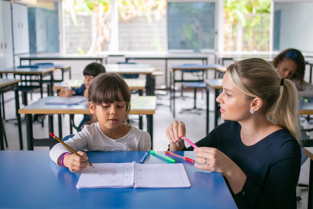 serious primary school teacher helping girl cope with her task 1