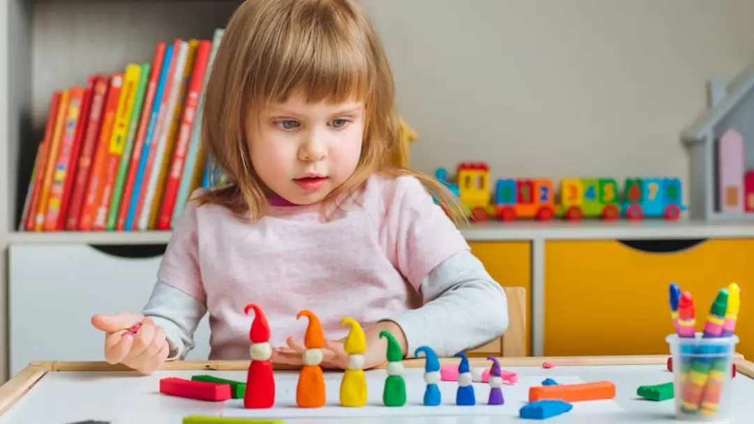 Play schemas autism, a young girl arranges plastic gnomes by size in a brightly lit playroom.
