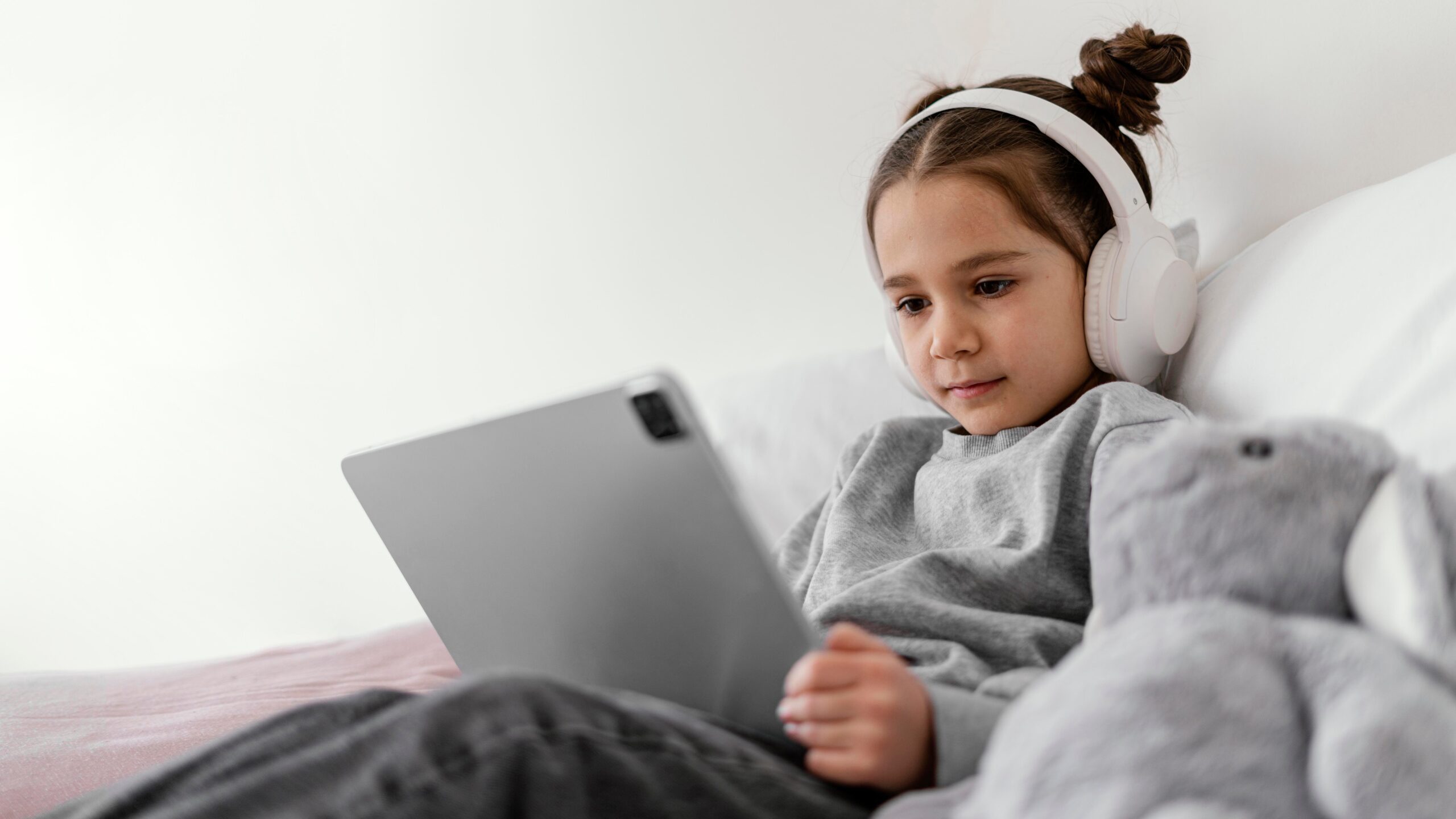 little girl bed with headphones using tablet 1 scaled