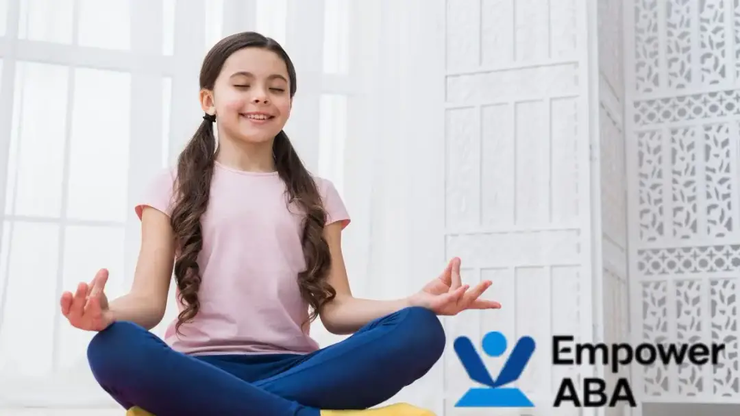 A young girl sits on the floor in a brightly lit white room, meditating near an autism calming sensory bubble tube.