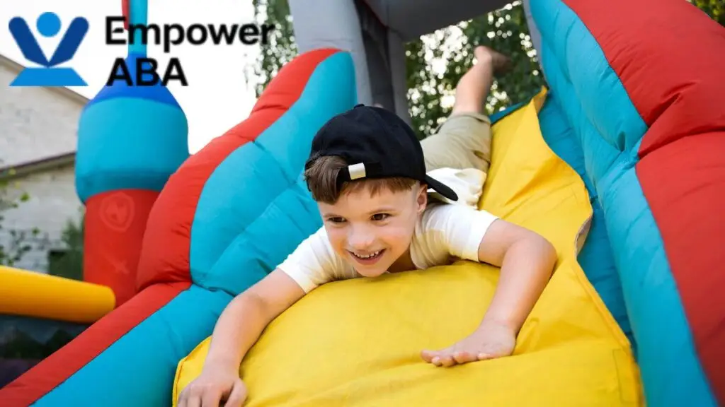 Autism vestibular therapy: a young boy enjoys sliding down a colorful bouncy house outdoors.