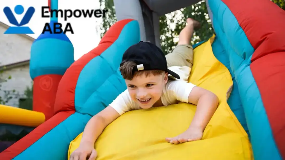 Autism vestibular therapy: a young boy enjoys sliding down a colorful bouncy house outdoors.