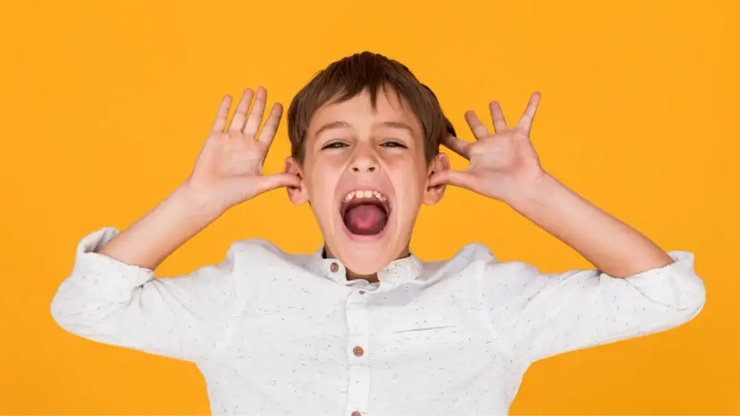 Autism vestibular therapy: a young boy expresses excitement, hands raised near ears, palms out.